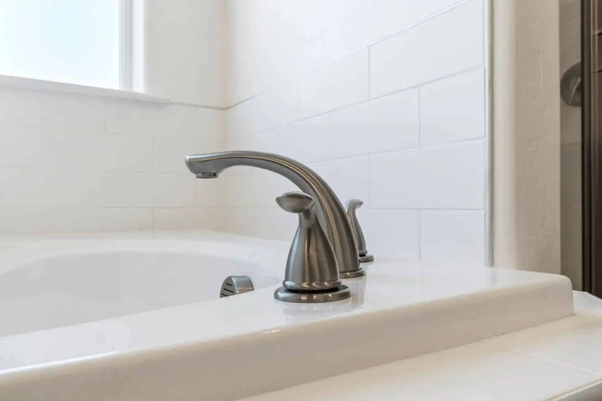 Bathroom sink faucet with white tiled wall background, close-up view.