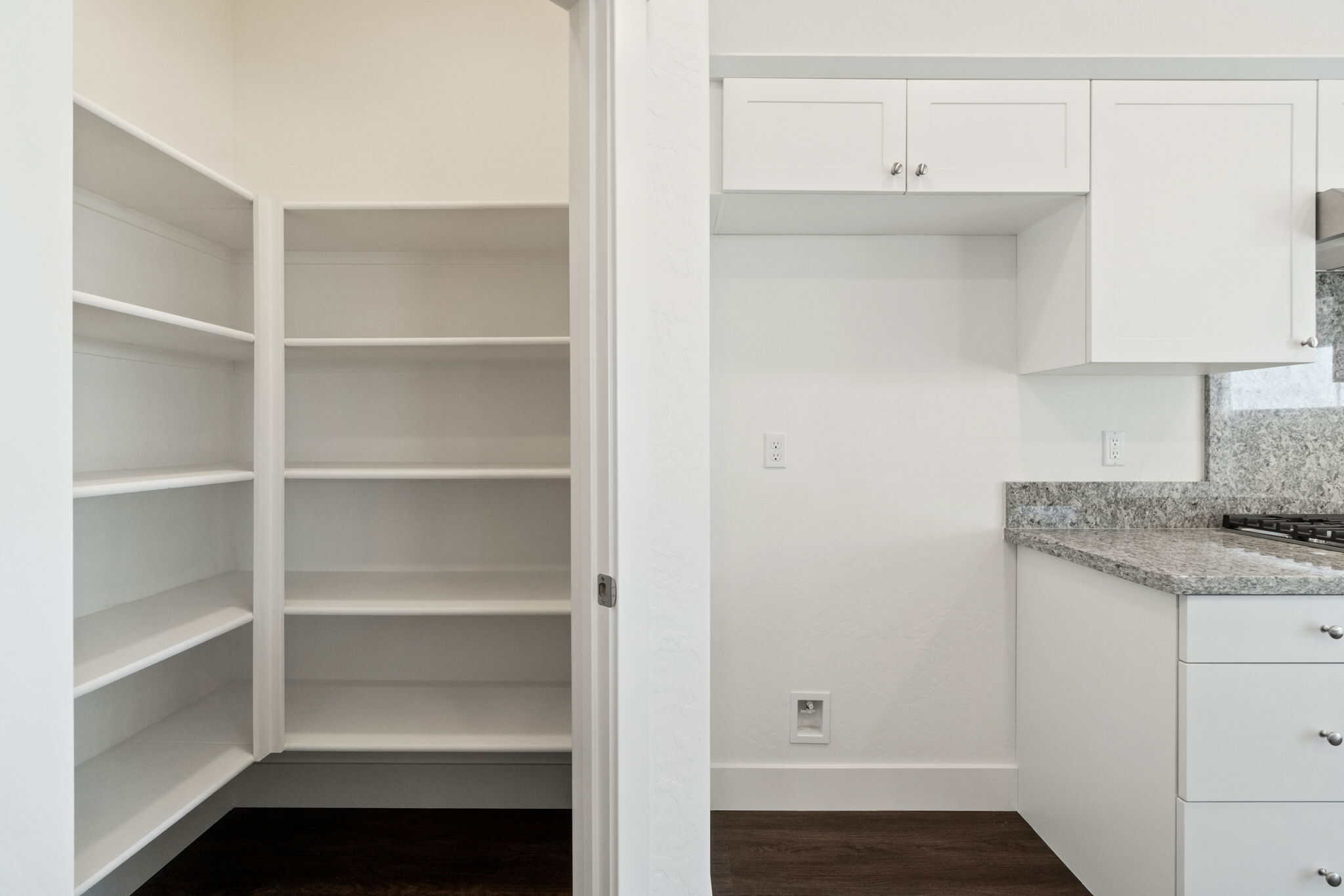 Empty closet and kitchen with white cabinets and granite countertops.