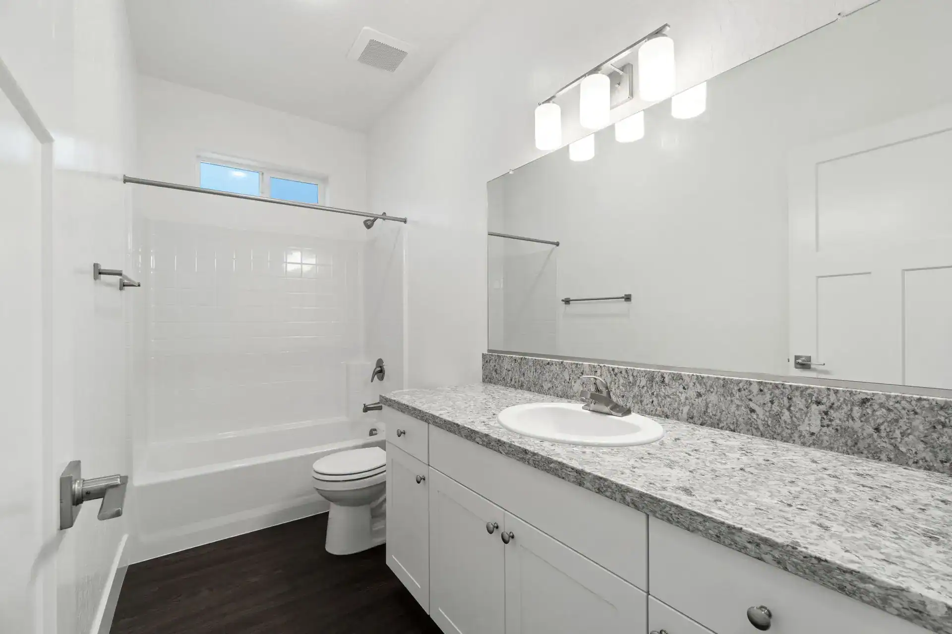 Modern white bathroom with granite countertop and shower enclosure.