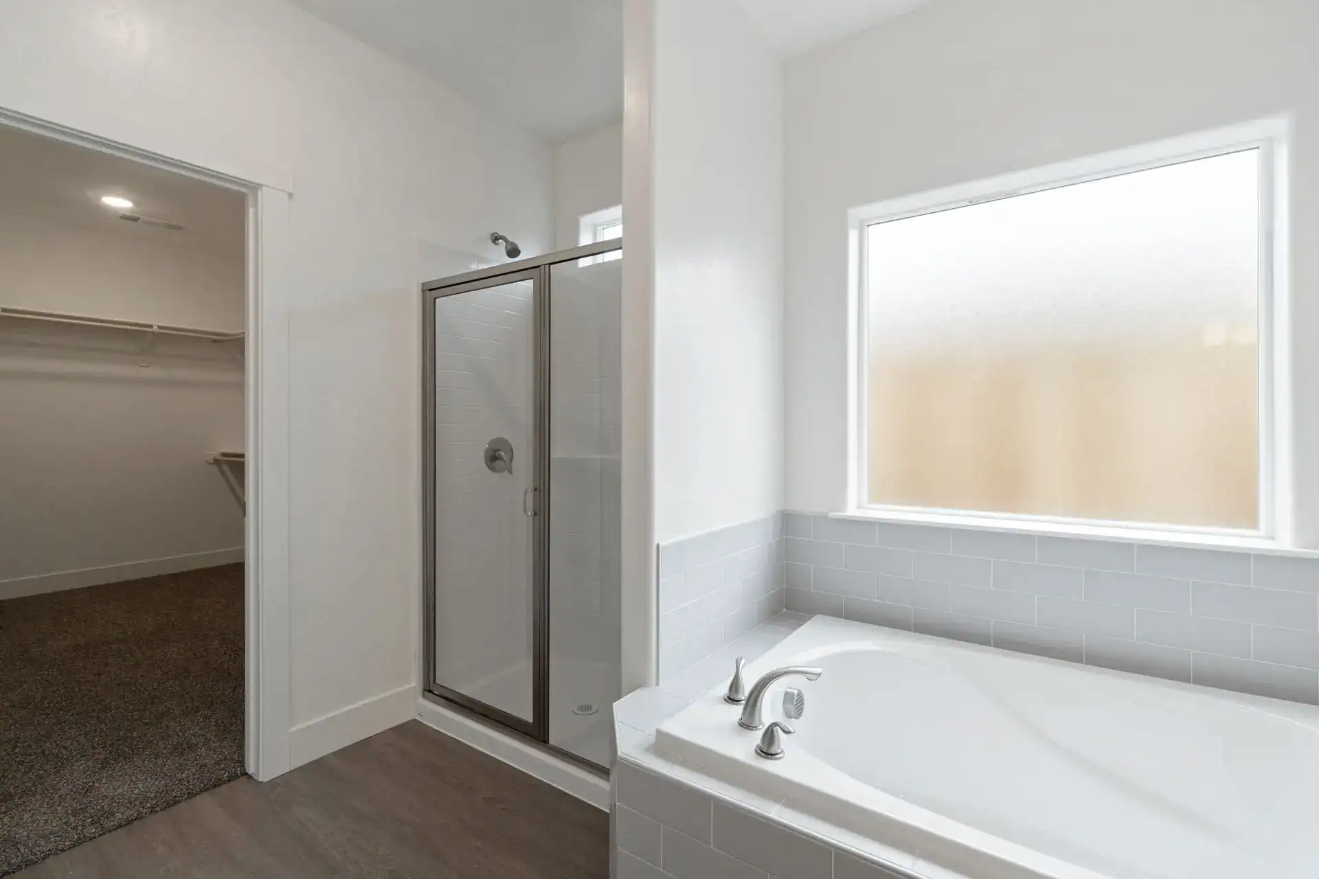 Bright bathroom featuring a glass shower enclosure and a large bathtub under a window.